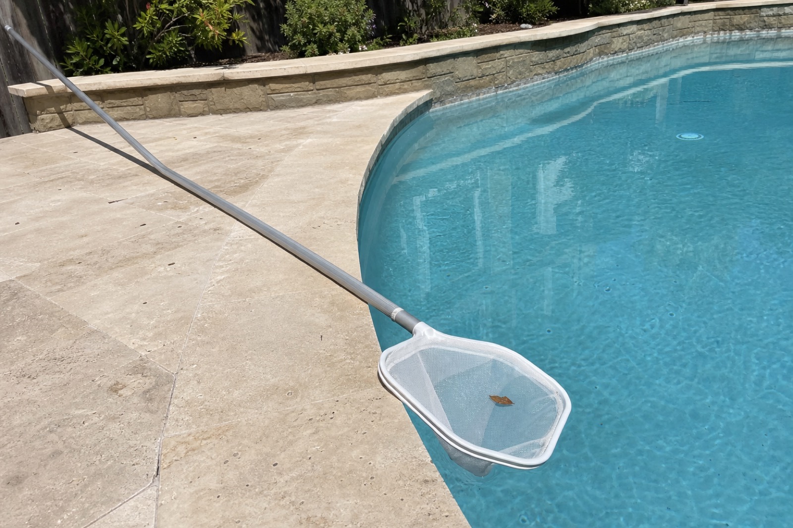 A skimming net resting across the edge of a clean residential pool with a single leaf in the net.